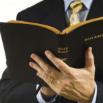 Gospel Sermon Triggers Criminal “Influence” Charge… Man in suit holding an open Holy Bible.