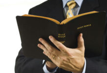 Gospel Sermon Triggers Criminal “Influence” Charge… Man in suit holding an open Holy Bible.