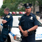 NEW Office Undermines NYPD — Who’s Really Running Safety? Two NYPD officers standing near a police car in an urban environment