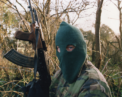shutterstock_1943493226.jpg Individual in camouflage holding a rifle, wearing a green balaclava