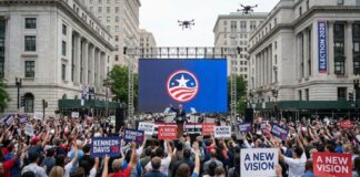 Crowd at a political rally holding signs and watching a speaker on stage