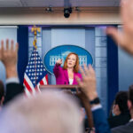 Outrage ERUPTS Over Democrat’s Zionist Camp PLAN Press secretary at podium, answering reporters questions, raised hands.