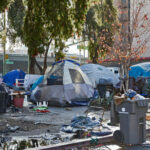 FAKE Homelessness Stunt SHOCKS L.A. Politician… Homeless encampment with tents and trash in urban area.