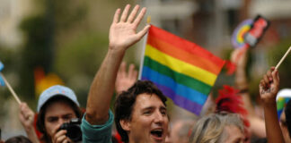 Man waving in a crowd with a rainbow flag in the background