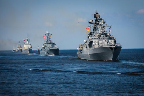 shutterstock_1465477688 Several naval warships sailing in the ocean.