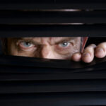 MUST SEE: Whatever HAPPENED To Rod Blagojevich? Man peeking through half-open black blinds.