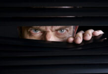 MUST SEE: Whatever HAPPENED To Rod Blagojevich? Man peeking through half-open black blinds.