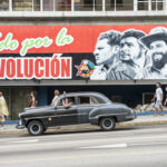 A mural depicting revolutionary figures with a classic car passing by