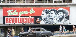A mural depicting revolutionary figures with a classic car passing by