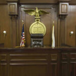 Ninth Circuit Judge BUSTED in BIZARRE Battery Case Judges bench in an empty courtroom, scales emblem above.