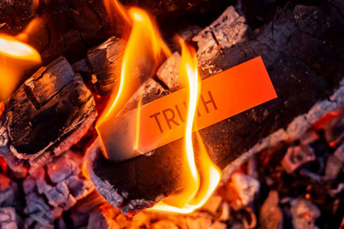 1908074851 Truth card burning in flames on charred wood.