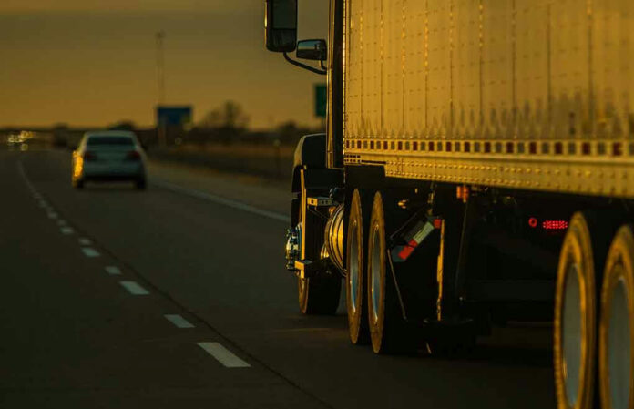 2289923583-1 Truck and car driving on highway at sunset.