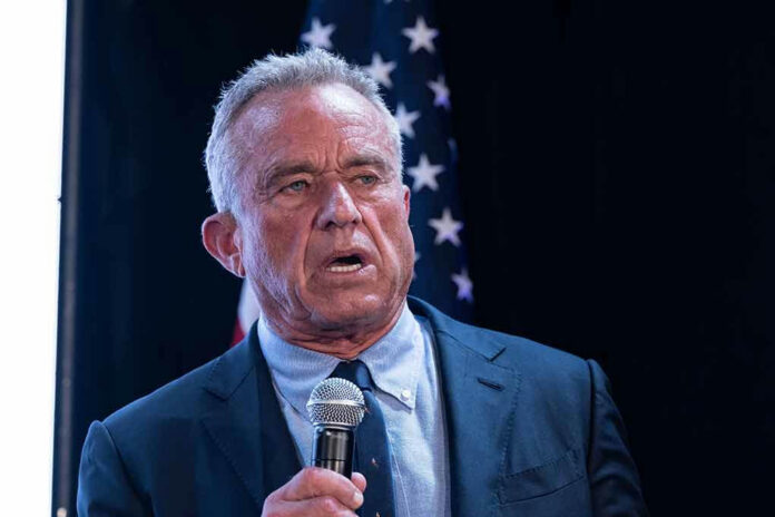 2456684675 Man in suit holding a microphone, American flag background.