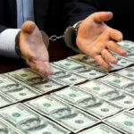 DOJ Raids Expose $6.5B Medicare Scam Handcuffed hands over a table of hundred-dollar bills.