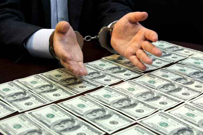 292760255-1 Handcuffed hands over a table of hundred-dollar bills.
