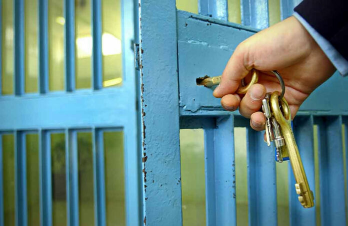 789621847 Hand unlocking a metal gate with keys.