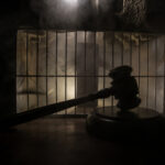 Court’s CRUSHING VERDICT — THIS is Now a Crime? A gavel placed on a wooden surface in front of a barred cage with a smoky background