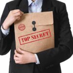 Person in suit holding a large brown envelope labeled top secret