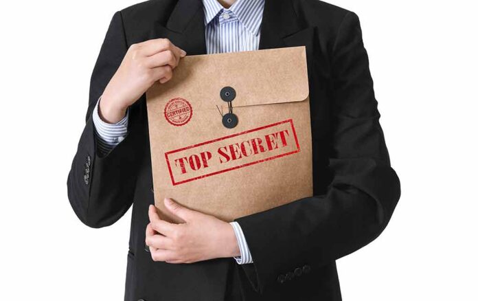shutterstock_2159470289-2-1- Person in suit holding a large brown envelope labeled top secret