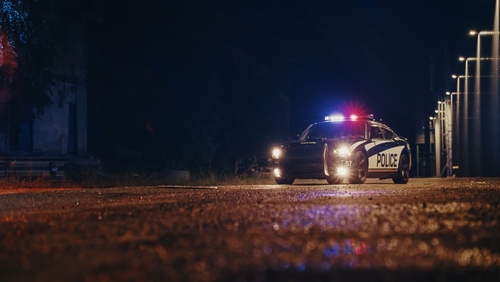Low,Angle,Shot,Of,A,Stopped,Police,Car,With,Lights Police car with flashing lights parked in a dark urban area