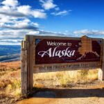 RURAL Patients Caught In Alaska CROSSFIRE Welcome to Alaska sign in a mountainous landscape