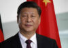 Trump Alleges Data Heist — Beijing Blasts Man in suit standing before Chinese flag.