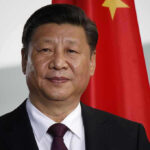 Trump Alleges Data Heist — Beijing Blasts Man in suit standing before Chinese flag.