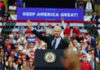 Politician speaking at rally with Keep America Great! sign.