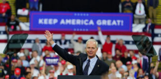 Politician speaking at rally with Keep America Great! sign.