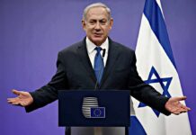 City Hall Bluff Exposed In Netanyahu Fight man in suit speaking at a podium with Israeli flag