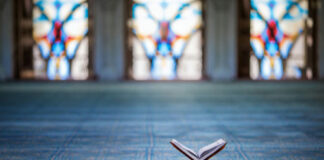 Quran on stand inside mosque with stained glass windows.