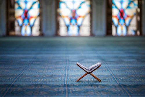 shutterstock_1074346307 Quran on stand inside mosque with stained glass windows.