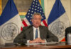 Man speaks at a press conference with flags behind.