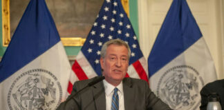Man speaks at a press conference with flags behind.