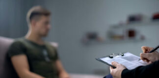 Therapist taking notes while talking with a young man.