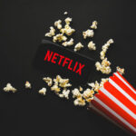 Woke Disclaimer Hijacks Hollywood Icon Spilled popcorn, phone displaying Netflix logo, striped popcorn container.
