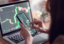 person analyzing stock charts on smartphone and laptop