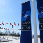 Delinquent Allies? Trump Turns Screws NATO flags displayed at the headquarters under a clear blue sky