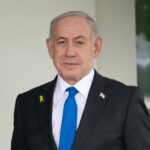 Netanyahu Claims “My Plan” Inside NDAA Man in suit speaking at a meeting table.