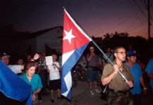Decades-Long Infiltration — U.S. Blindsided A group of people participating in a protest march holding a Cuban flag