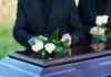 Placing white roses on a wooden coffin.