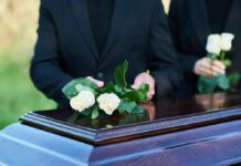 Placing white roses on a wooden coffin.