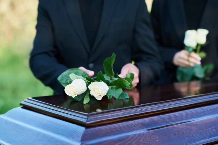 Placing white roses on a wooden coffin.