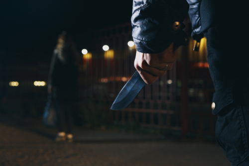 Man holding knife standing behind unaware person.