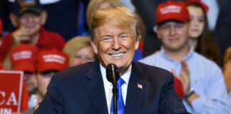 A man speaking at rally with supporters in background.