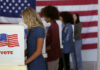 People voting in booths with U.S. flags in background.