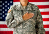 Soldier saluting in front of an American flag.