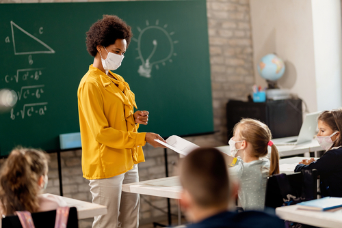 Teacher interacting with masked students in classroom.