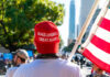 Person in MAGA hat holding U.S. flag at rally.