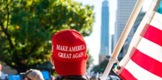 Person in MAGA hat holding U.S. flag at rally.